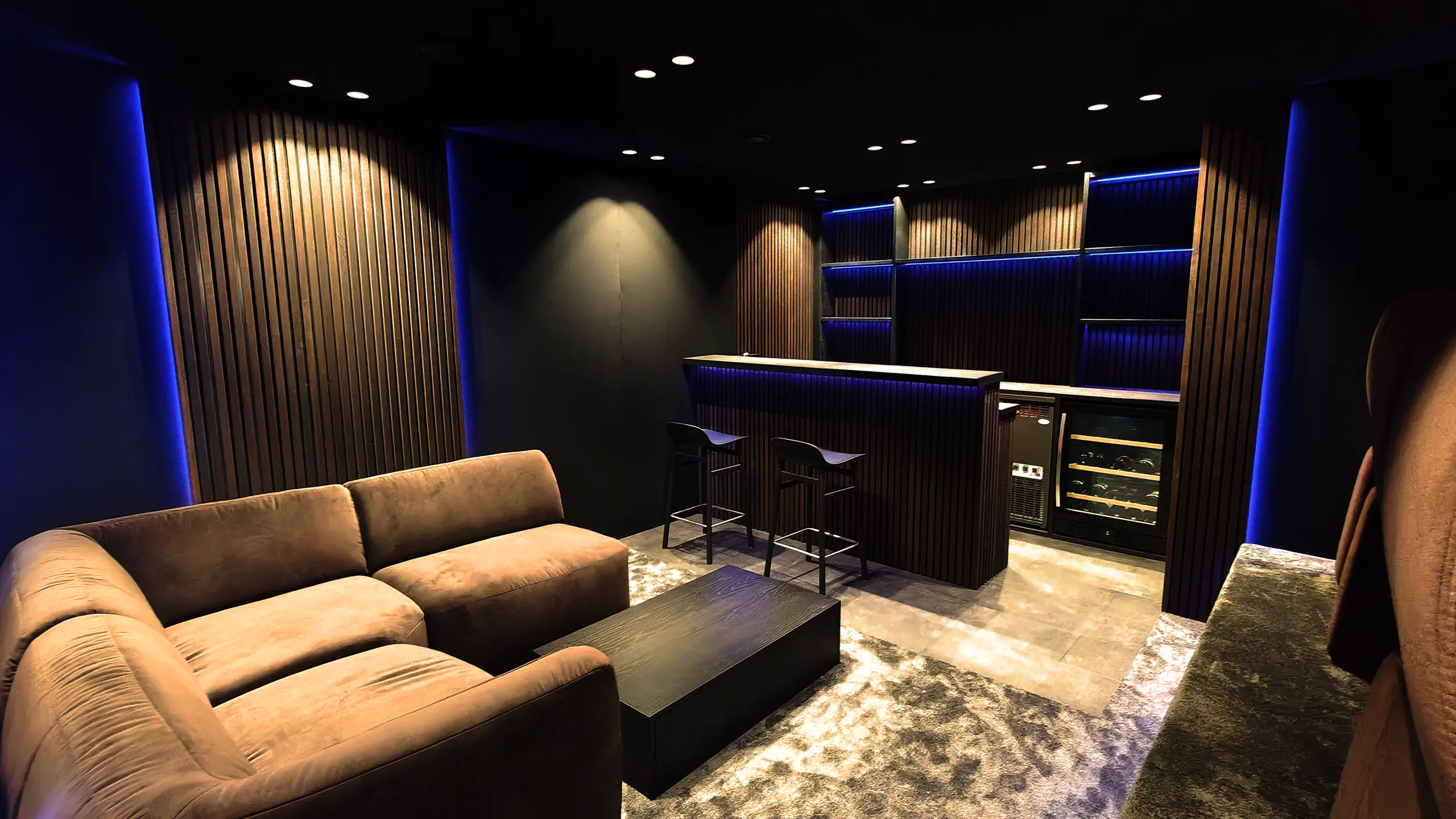 Bar og lounge ved hjemmebiografen med sofa, barstole, belyste hylder og vinkøleskab
